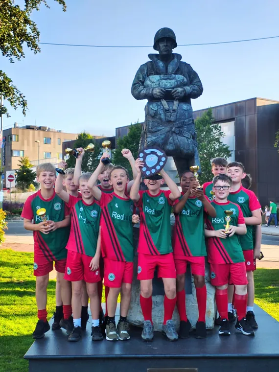 Ash United youth players celebrating with the league shield in RedteQ-sponsored kit