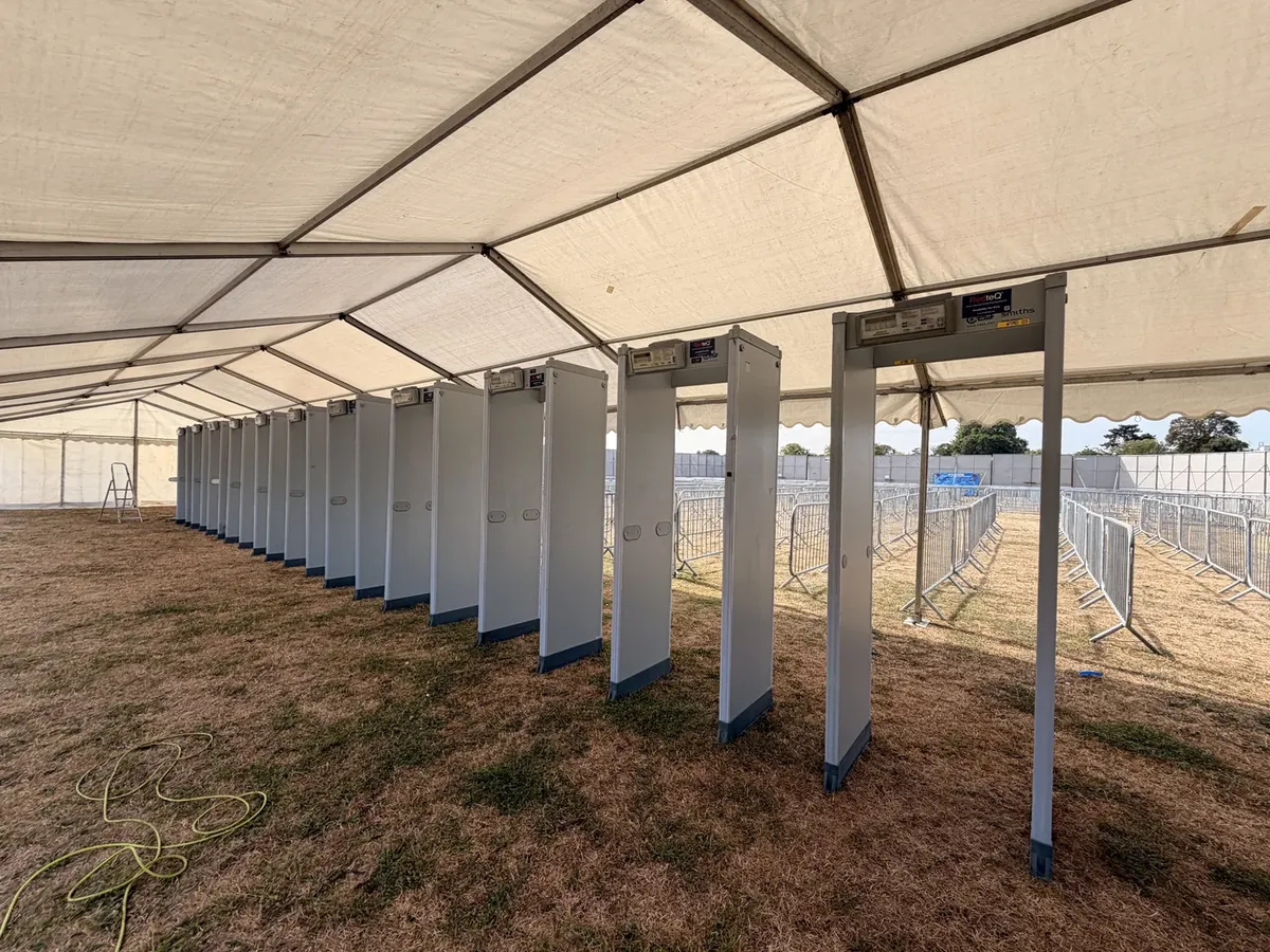 A long row of walk-through metal detectors under a marquee at a UK music festival gate